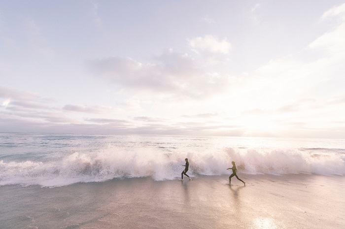 People walking in ocean surf under a sunset