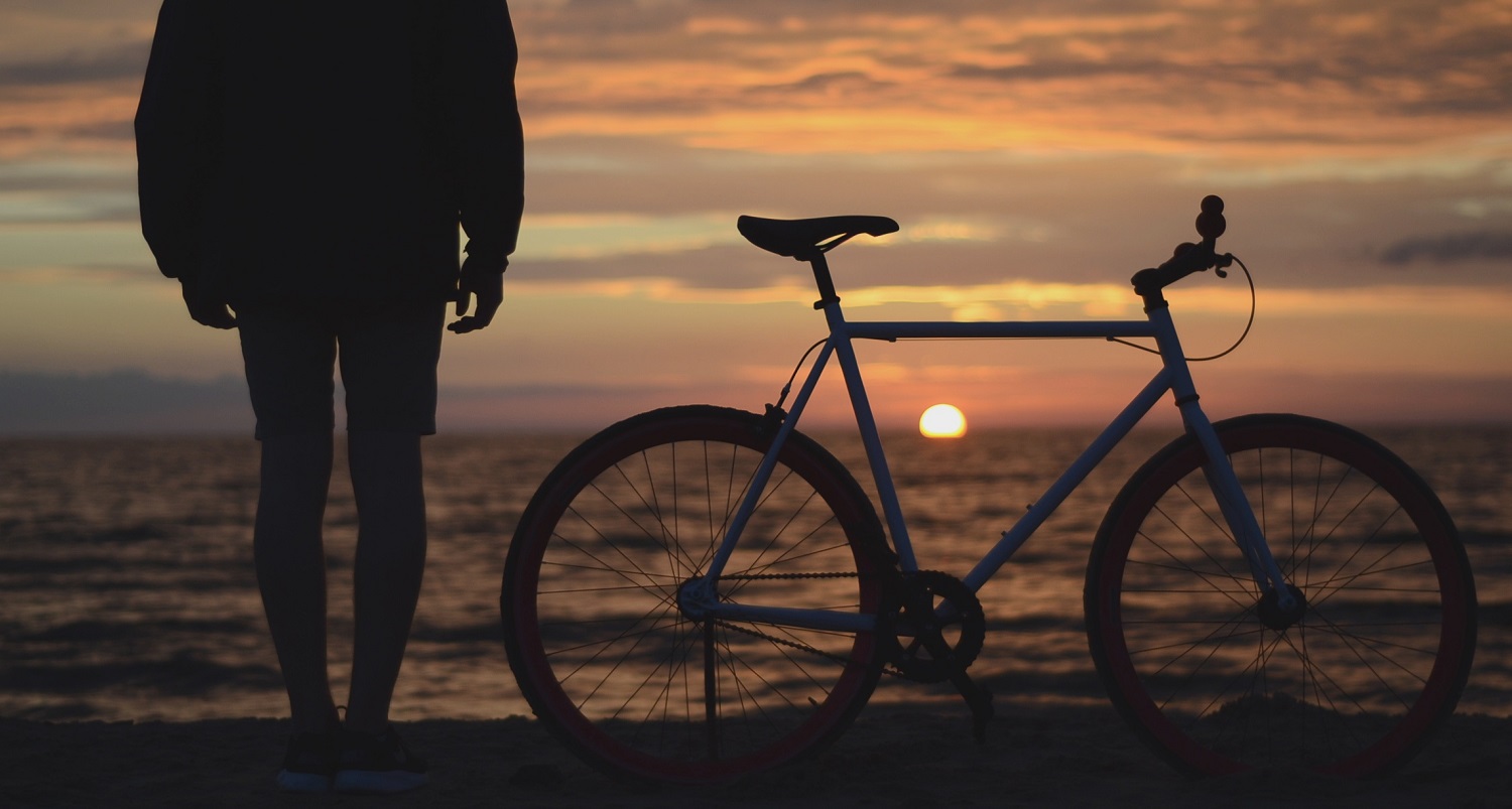 photo of man with bike at sunset